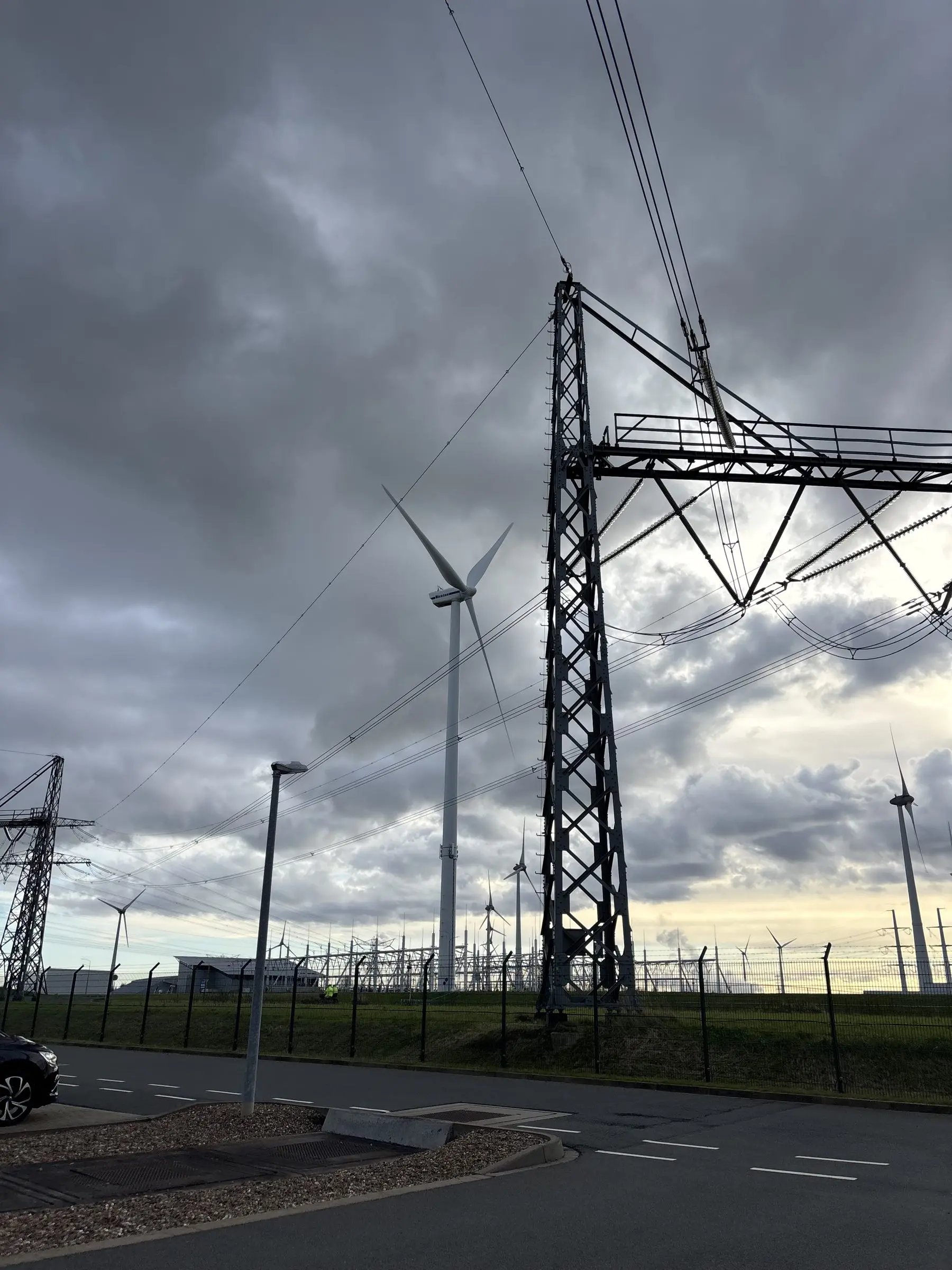 High-voltage pylon and wind turbines under a stormy sky
